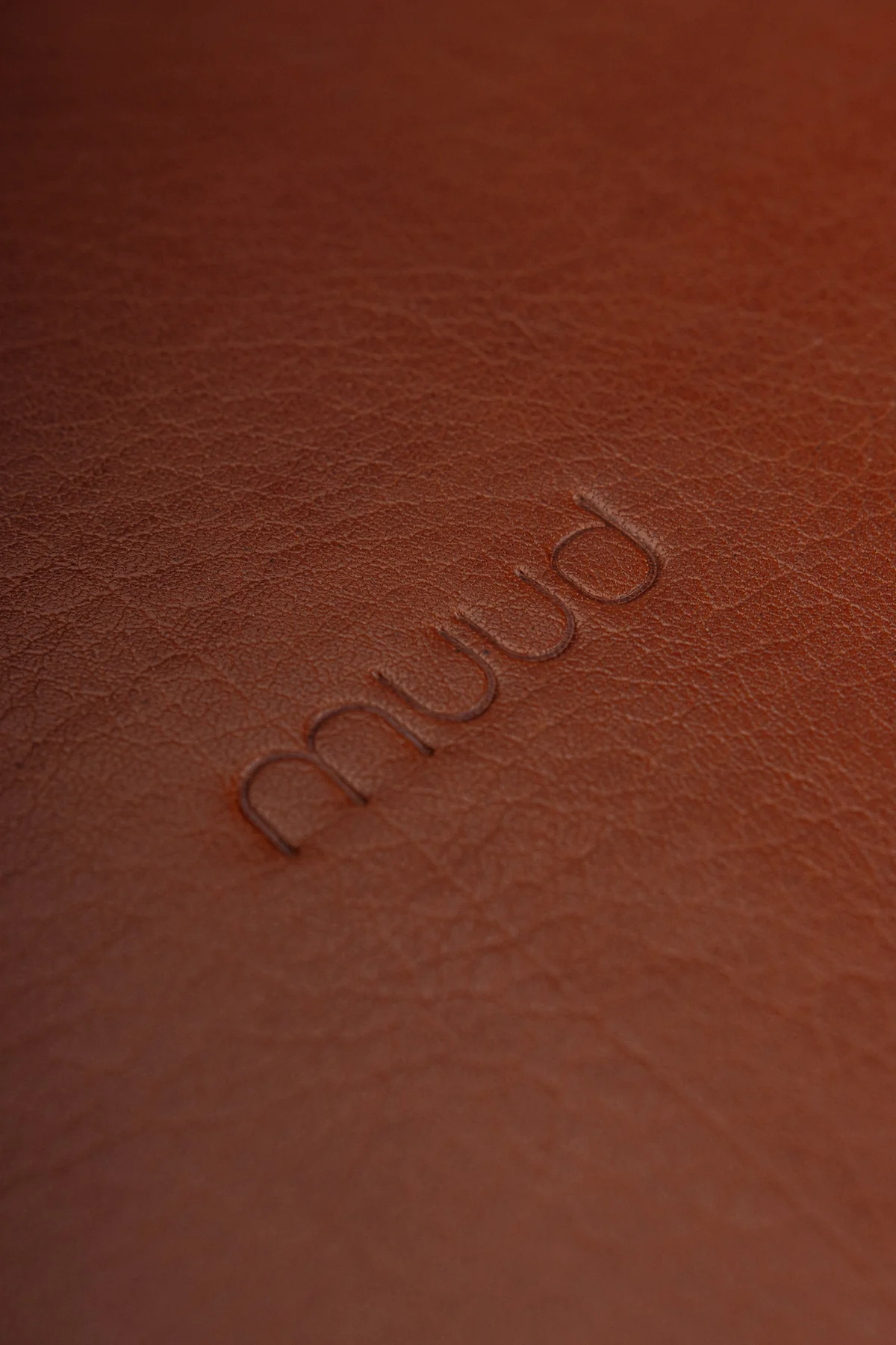 Nærbilde av preget muud-logo på Muud Duff rund lærdetalj i rich brown skinn – Diro Design